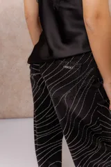 Pantalón wide leg de tiro alto en denim negro, con diseño de líneas onduladas formadas por pequeñas aplicaciones de brillos. Cuenta con cierre frontal, bolsillos funcionales y pasacintos.