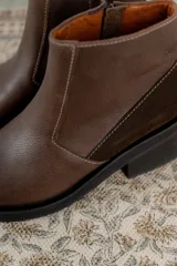 Bota corta de cuero marrón con panel trasero de gamuza en tono más oscuro, suela de goma negra y taco cuadrado bajo.