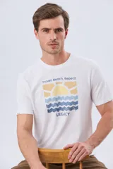 Remera blanca de manga corta y cuello redondo, con estampa frontal inspirada en el mar y atardeceres de verano con la inscripción 'Travel. Beach. Repeat.' y 'Legacy'.