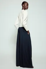 Pantalón de tiro medio de corte wide leg, confeccionado en mezcla de lyocell con patrón de rayas diplomáticas. Presenta bolsillos laterales ocultos, pliegues delanteros marcados y cierre frontal con cremallera, botón y ganchos metálicos.