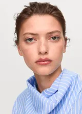 Blusa de manga larga con diseño de rayas verticales en tonos azul y blanco. Presenta un cuello redondo con un pañuelo integrado que cae sobre el pecho y puños abotonados.