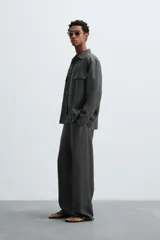 Pantalón de corte relajado confeccionado en tejido de cáñamo color blanco roto. Presenta cintura elástica con cordón interior ajustable, cierre frontal con botones, bolsillos laterales y un bolsillo trasero de plastrón.