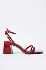 Sandalias de tacón cuadrado medio, color rojo charol, con diseño de tiras finas en el empeine y cierre de pulsera con hebilla al tobillo. Presentan punta cuadrada.
