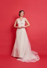 Vestido de novia largo color blanco, sin mangas, confeccionado en organza de seda natural con tul que cubre los hombros y extensa cola de tul que comienza desde la espalda con corte en V.