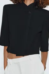 Blazer cropped de corte estructurado, con cuello subido, manga corta y cierre frontal con un botón. Presenta un bolsillo de vivo en el pecho y forro interior a tono.