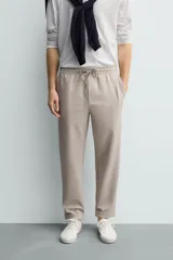 Pantalón jogger color beige de tejido transpirable y elástico con cintura elástica ajustable con cordón, bolsillos frontales y bajo con vuelta.