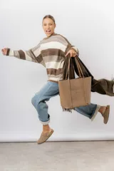 Bolso tipo tote de color marrón, confeccionado en material símil cuero texturado. Presenta un diseño estructurado con asas largas para llevar al hombro y el logo de la marca aplicado en la parte frontal.