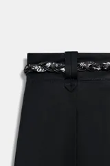 Pantalón de popelina de tiro alto y pernera ancha, de color negro. Presenta pinzas delanteras, bolsillos laterales y falsos bolsillos de vivo en la espalda. Incluye un cinturón combinado tipo pañuelo trenzado con tiras colgantes y cuentas de madera. Cierre frontal con cremallera, botón interior y gancho.