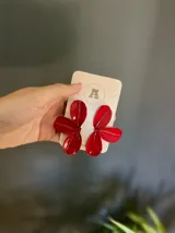 Par de aros colgantes con forma de flor de cuatro pétalos esmaltados en color rojo.