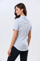 Camisa celeste rayada de manga corta, con cuello camisero y cierre frontal con botones. Presenta un corte entallado y un pequeño detalle de placa metálica en el borde inferior.