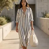 Vestido camisero maxi de corte holgado y manga larga, con diseño a rayas verticales en tonos azul y blanco, cuello camisero y escote en V.