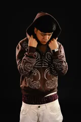 Hoodie con cierre frontal, color marrón, con diseño estampado de hojas de acanto en color blanco que recorre el frente y las mangas. Cuenta con bolsillos laterales y costuras visibles.