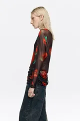 Camiseta de tul de manga larga con escote barco, diseño ajustado y efecto fruncido en los laterales del bajo. Presenta un estampado de flores rojas sobre fondo oscuro.