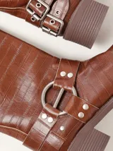 Botas de caña media confeccionadas en cuero texturado color marrón. Presentan un diseño robusto con múltiples hebillas metálicas ajustables, apliques circulares laterales y punta cuadrada. Cuentan con un taco cuadrado de 5 cm de altura.