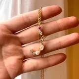 Cadena dorada con dije de letra grande, con piedras y perlas engarzadas.