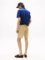 Pantalón corto tipo bermuda de sarga de algodón elástico, color beige, con cierre de cremallera, bolsillos delanteros y traseros, e incluye cinturón con detalles distintivos.