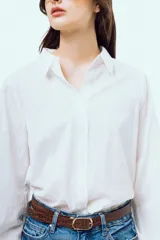 Camisa blanca de manga larga con sutil patrón de rayas verticales, cuello camisero, cierre frontal con botones y puños elásticos.