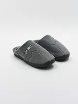 Pantufla gris con diseño acolchado en forma de rombos imitando un balón de fútbol, con la palabra "SPORT" bordada en el lateral y suela de goma.