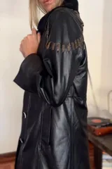 Tapado largo de cuero negro con cuello de piel sintética desmontable y detalles de pasamanería marrón vintage en hombros y espalda. Se convierte en abrigo corto mediante un cierre.