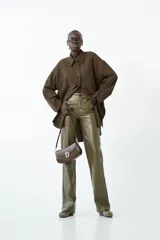 Camisa larga de manga larga, color marrón oscuro, con cuello camisero y botones frontales. Presenta un corte holgado y frunce sutil en las mangas.