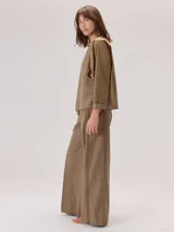 Camisa de manga larga con diseño bicolor en tonos tierra. Presenta un panel frontal y trasero en color beige, contrastado con mangas de un tono marrón más oscuro y textura satinada. Posee cuello redondo y corte recto.
