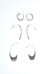 Set de tres pares de aros plateados de diseño variado, incluyendo aros de argolla texturados, aros colgantes alargados y aros con dijes en forma de medialuna.