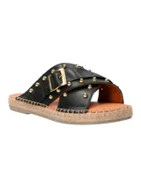 Sandalias planas negras con tiras cruzadas de cuero, tachas doradas, hebilla metálica y detalle de yute en la suela.
