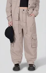 Pantalón cargo de corte oversize y silueta estructurada, color beige. Confeccionado en microfibra pesada, cuenta con cintura elástica con cordón de ajuste, cierre frontal con botón, bolsillos laterales y bolsillos cargo de gran tamaño con tapa y broches a presión.