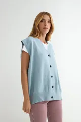 Chaleco de punto color verde, con escote en V y cierre frontal de botones negros. Presenta un diseño holgado con terminaciones acanaladas en el cuello, sisas y ruedo.