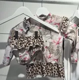 Conjunto de lycra con protección UV, estampado con hojas de palmera y animales de la selva. Incluye remera de manga larga con volados en los hombros y bombacha con volados en la cintura.