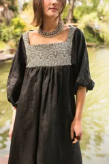 Túnica de lino color negro con corte holgado y mangas abullonadas con puños elásticos. Presenta una pechera cuadrada en el frente y la espalda confeccionada en textil antiguo con estampado geométrico en tonos blanco y negro.