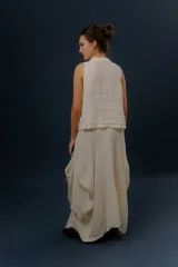 Pollera larga de lino color gris topo, de diseño amplio con volumen, movimiento y bolsillos delanteros. Cuenta con elástico en la cintura y detalles de pinzas y sobretelas en los laterales.