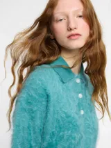 Sweater de punto de cachemira color turquesa con cuello polo y cierre frontal de tres botones. Presenta una textura suave tipo pelo, manga larga y terminaciones acanaladas en puños y ruedo.