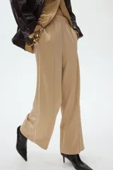 Pantalón de punto color beige con cintura elástica fruncida, piernas amplias, pliegues delanteros y ribetes laterales en color blanco.