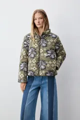 Campera puffer color verde militar con estampado floral grande y detalles geométricos, cuello alto y cierre frontal con cremallera.