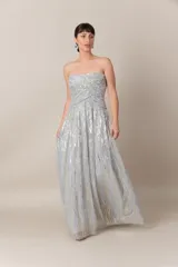 Vestido largo de tul bordado color gris claro, con lentejuelas plateadas y doradas. Modelo strapless drapeado y falda con movimiento.
