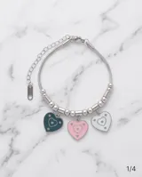 Pulsera de cadena de acero con eslabones tipo bolita y tres dijes colgantes en forma de corazón con esmalte en colores pastel: rosado, blanco y turquesa.