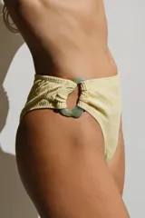 Bottom de bikini color amarillo pálido, modelo vedetina con argolla decorativa verde agua en el lateral.