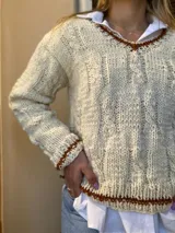 Sweater tejido a mano en lana color crudo, con cuello redondo y terminaciones en punto marrón.