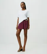 Short pollera de sastrería marca Cortelle, color bordó, confeccionado en crepé. Presenta sobreposición frontal efecto pollera con pliegues y detalle de cadena metálica decorativa en el lateral.