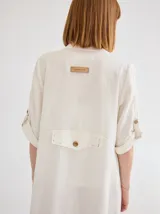 Vestido camisero midi de lino color beige, con diseño de manga corta con solapa, cuello camisero, bolsillo trasero con solapa y botón, y aberturas laterales en el ruedo.