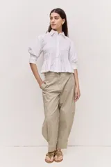 Camisa blanca de cuello clásico y mangas abullonadas tres cuartos, con diseño fruncido en el frente, calce amplio y ruedo estilo peplum.