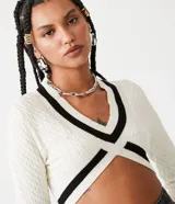 Suéter cropped de punto texturizado color crema, con escote en V y detalles a contraste en negro en mangas, cuello y busto.