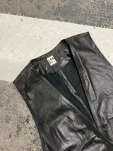 Chaleco de cuero negro, abierto a los costados, con tiras que se regulan a necesidad y gusto de cada una. Presenta bolsillos frontales y escote en V.