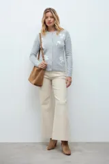 Cardigan de punto color gris melange con cuello redondo, cierre frontal de botones y delicado bordado floral en color blanco en la parte frontal.