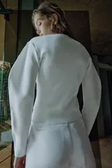 Chaqueta de punto de cuello redondo y manga larga, en color blanco, con cierre frontal asimétrico de botones negros.