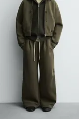 Pantalón de corte wide fit confeccionado en tejido técnico compacto con efecto neopreno. Presenta cintura elástica con cordón ajustable, pliegues frontales, bolsillos laterales y detalle de pliegues en las rodillas con aplicaciones metálicas.