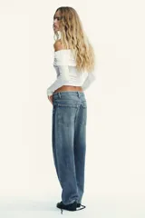 Jeans de tiro medio con diseño baggy barrel, cinco bolsillos y costuras laterales torcidas. Presenta cierre frontal con cremallera y botón metálico.