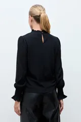 Blusa de color rojo con cuello alto y detalle de volados, mangas largas con puños elásticos en punto smock y textura sutil en la tela.