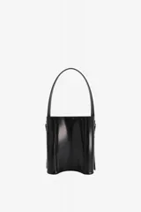 Bolso de mano tipo cubo color negro, de diseño estructurado y cilíndrico, confeccionado en cuero vacuno con acabado brillante. Cuenta con asa superior fija y correas laterales decorativas con hebillas metálicas plateadas.